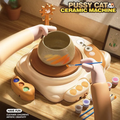 Cat pottery wheel in use: a cream cat-shaped electric wheel with a clay bowl on the turntable being painted, paint pots and brushes beside it